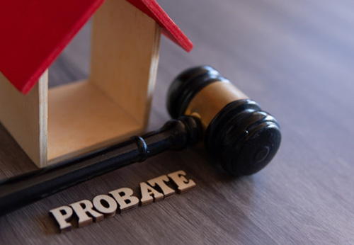 A small wooden model of a house, a gavel, and wooden letters spelling PROBATE on a dark wood surface.