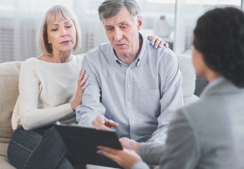 An elderly couple discusses documents with a professional in a bright, modern setting.