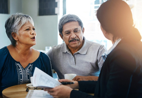 An elderly couple consults with a professional who is showing them information on a tablet.